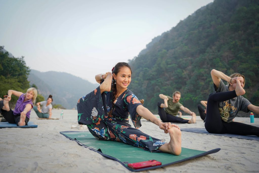 Group practicing yoga on a serene beach in Bali, Indonesia, surrounded by lush hills.