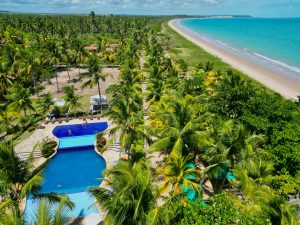 Aerial photo featuring a tropical poolside at a lush beachfront resort with palm trees and pristine ocean.
